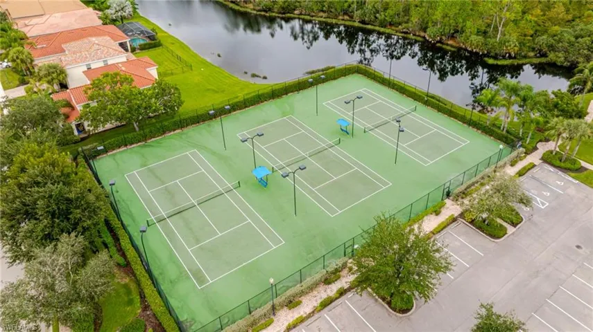 Four tennis courts with perimeter fencing, sports lighting, and a paved parking area
