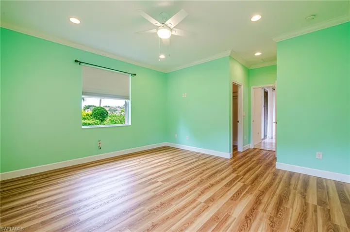 Wood-finish flooring, recessed lighting, ceiling fan, crown molding, and window with roller shade
