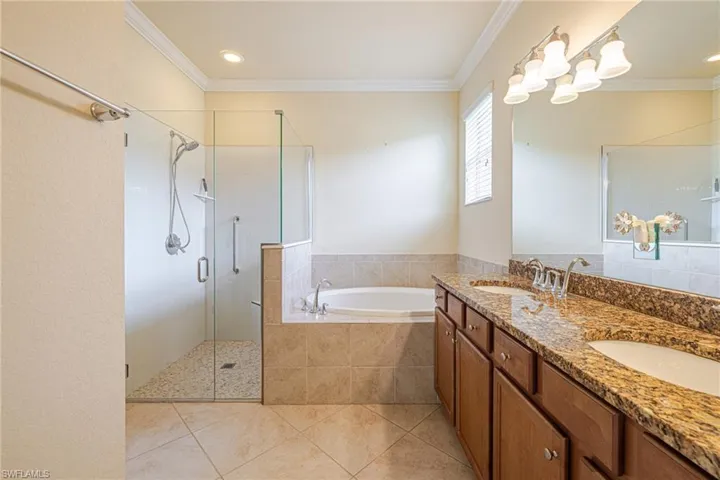 Dual vanity with stone countertop, tile flooring, glass-enclosed shower, built-in bathtub, and crown molding