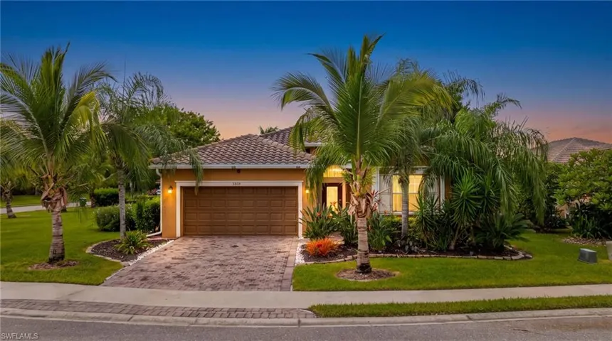 Exterior featuring a tiled roof, stucco finish, paver driveway, mature palm trees, and lush landscaping