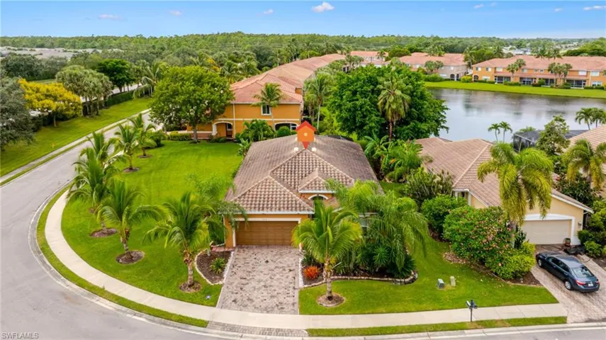 Corner lot residence with a paver driveway, terracotta-style roof, mature landscaping, and an attached garage
