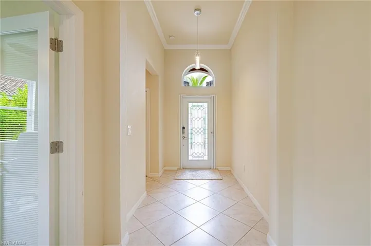 Tiled flooring, crown molding, a decorative glass entry door, an arched transom window, and a contemporary pendant light fixture