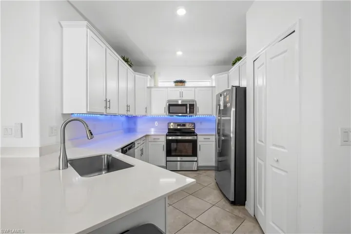 Contemporary kitchen featuring stainless steel appliances, white cabinetry, a single basin sink with a gooseneck faucet, light-toned countertops, and tile flooring