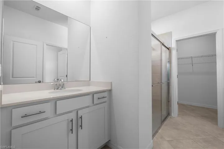 Master Bathroom Continuationfeaturing a dual vanity with light-toned countertop, a frameless mirror, and a glass-enclosed shower