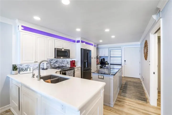 Kitchen with light hardwood / wood-style flooring, kitchen peninsula, stainless steel appliances, backsplash, and sink
