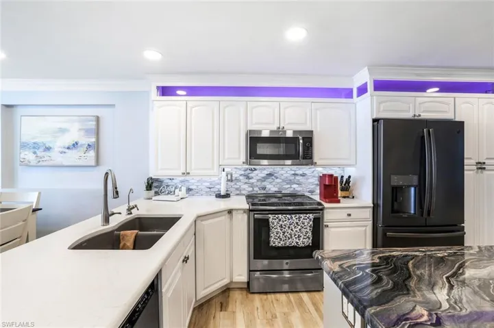 Kitchen featuring light wood-type flooring, appliances with stainless steel finishes, white cabinets, backsplash, and sink
