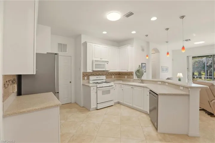 Kitchen featuring decorative backsplash, stainless steel appliances, a peninsula, and white cabinetry
