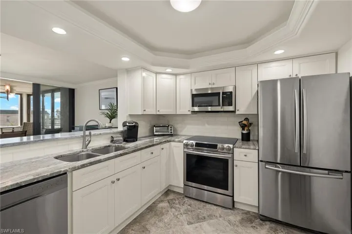 Kitchen with stainless steel appliances, sink, white cabinets, and a tray ceiling