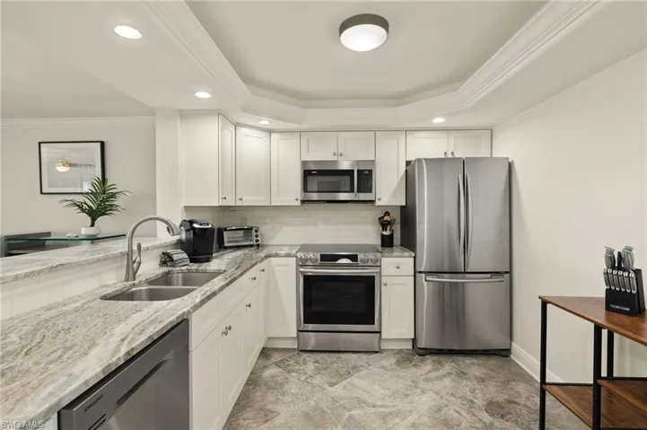 Kitchen featuring sink, a tray ceiling, stainless steel appliances, light stone countertops, and white cabinets