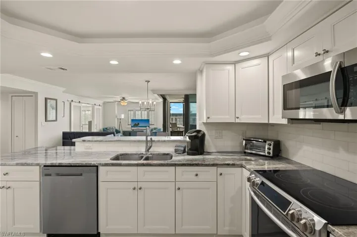 Kitchen featuring sink, appliances with stainless steel finishes, white cabinets, decorative backsplash, and kitchen peninsula