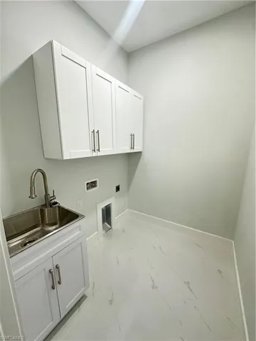 Clothes washing area featuring hookup for a washing machine, sink, electric dryer hookup, and cabinets
