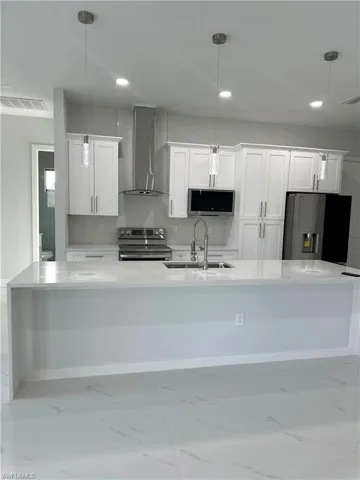Kitchen with wall chimney exhaust hood, stainless steel appliances, and decorative light fixtures