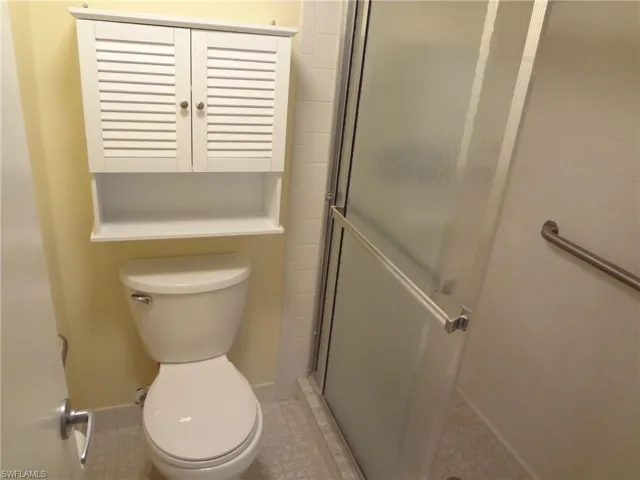 Bathroom featuring tile patterned flooring, dual sinks, tile walls, a shower with door, and toilet