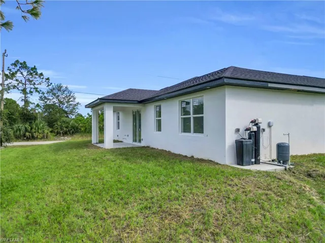 Back of house featuring a patio area, a lawn, stucco siding, and roof with shingles