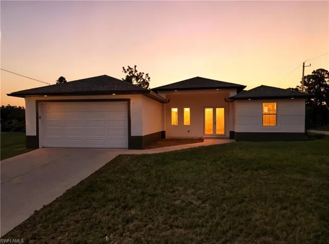 View of front facade with stucco siding, driveway, a front lawn, and a patio area