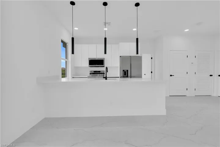 Kitchen with white cabinetry, a peninsula, stainless steel appliances, modern cabinets, and light stone counters
