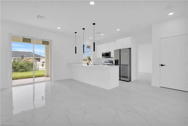 Kitchen featuring light marble finish floors, stainless steel appliances, a peninsula, decorative light fixtures, and white cabinets
