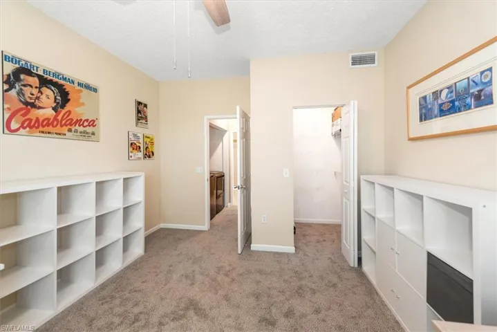 Bedroom featuring a textured ceiling, newer light colored carpet, a ceiling fan, and a walk in closet