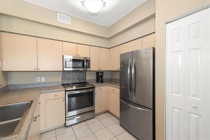 Kitchen featuring newer stainless steel appliances, light wood finish cabinetry, and light tile patterned floors