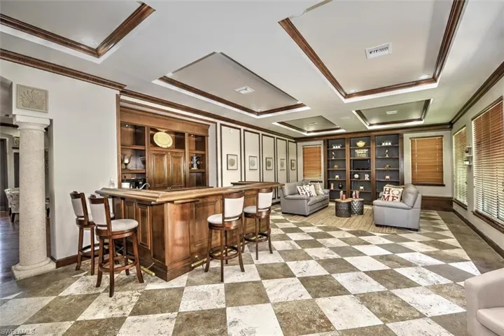 Club room with bar featuring decorative columns, ornamental molding, and coffered ceiling