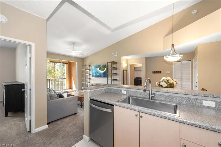 Kitchen with open floor plan, light countertops, newer stainless steel dishwasher, light carpet, and vaulted ceiling