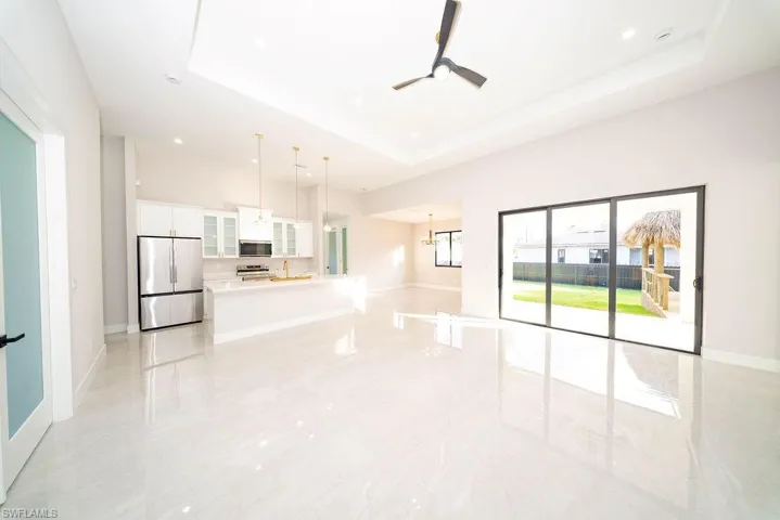 Unfurnished living room with ceiling fan, a chandelier, a tray ceiling, and light marble finish floors