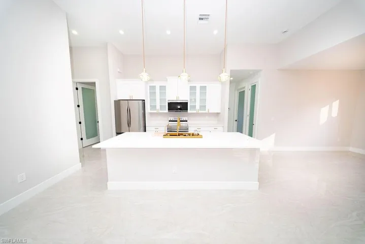 Kitchen featuring glass insert cabinets, white cabinets, appliances with stainless steel finishes, a large island with sink, and hanging light fixtures