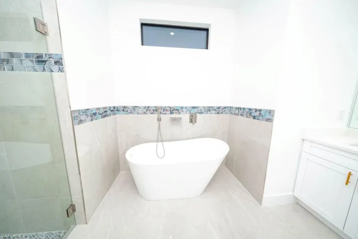 Bathroom featuring a freestanding bath, a shower stall, vanity, and tile walls