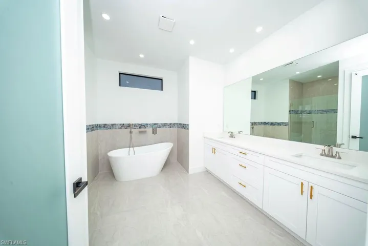 Bathroom featuring a shower stall, tile walls, double vanity, a freestanding tub, and a wainscoted wall