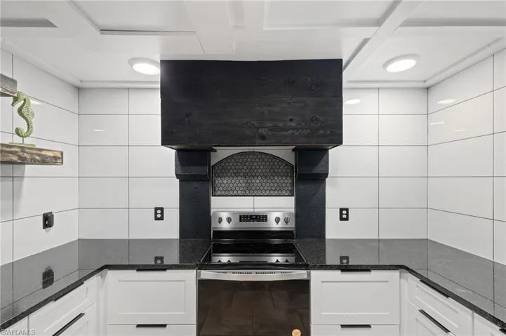 Kitchen with dark stone counters, white cabinetry, tile walls, and stainless steel range with electric stovetop