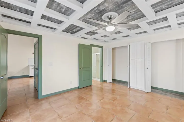 Unfurnished bedroom with coffered ceiling, light tile patterned floors, and ceiling fan