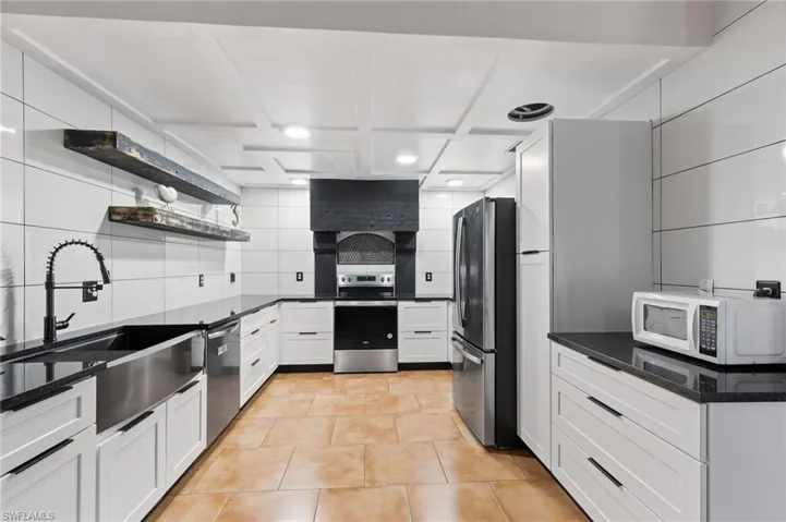 Kitchen with light tile patterned flooring, tasteful backsplash, white cabinets, stainless steel appliances, and sink