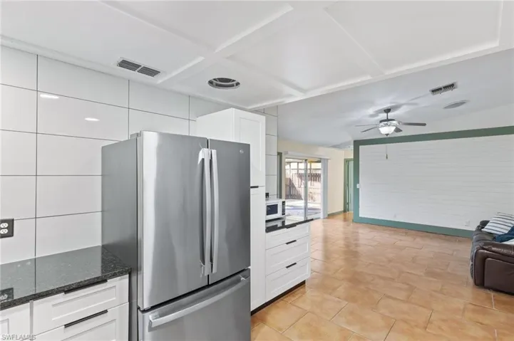 Kitchen featuring stainless steel fridge, dark stone counters, white cabinetry, and ceiling fan