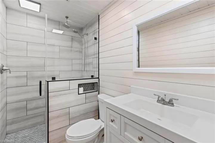 Bathroom featuring wooden walls, toilet, vanity, and an enclosed shower