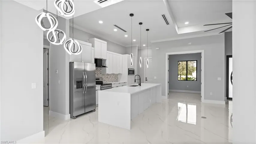 Kitchen featuring stainless steel appliances, ornamental molding, decorative backsplash, modern cabinets, and a kitchen island with sink