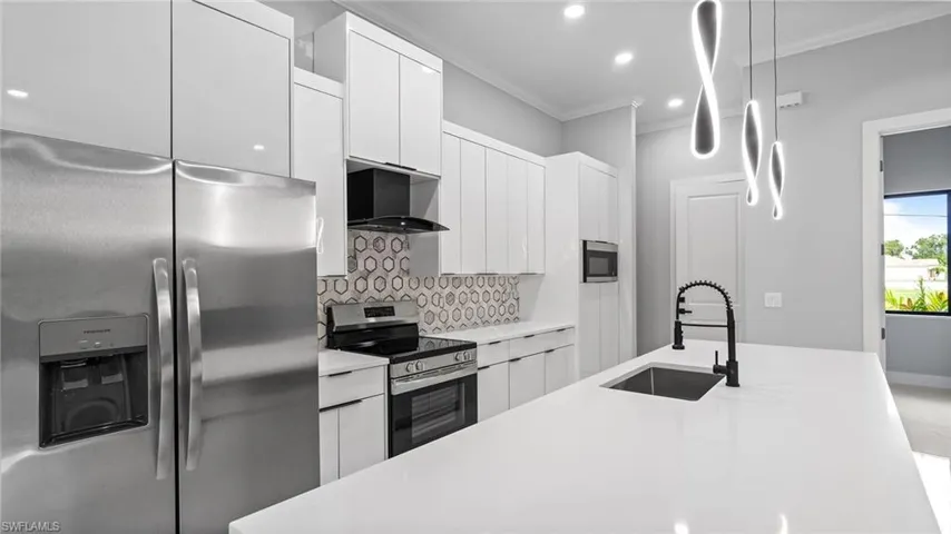 Kitchen with stainless steel appliances, ornamental molding, tasteful backsplash, light countertops, and white cabinetry