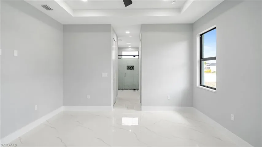 Empty room with light marble finish floors, a tray ceiling, recessed lighting, and a ceiling fan