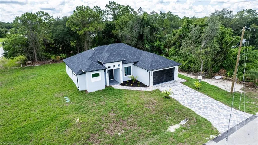 View of front of house featuring decorative driveway, a garage, a shingled roof, a front yard, and stucco siding