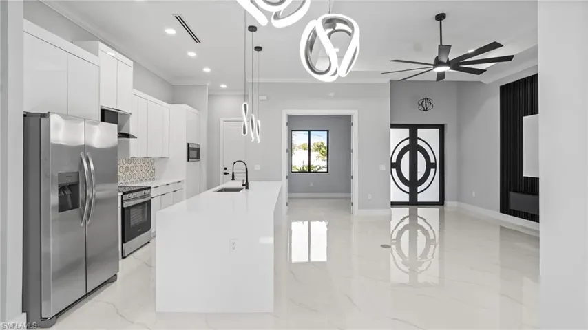 Kitchen with appliances with stainless steel finishes, light marble finish flooring, crown molding, white cabinetry, and an island with sink