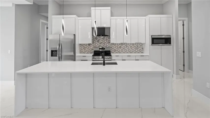 Kitchen with appliances with stainless steel finishes, white cabinets, modern cabinets, backsplash, and light marble finish flooring