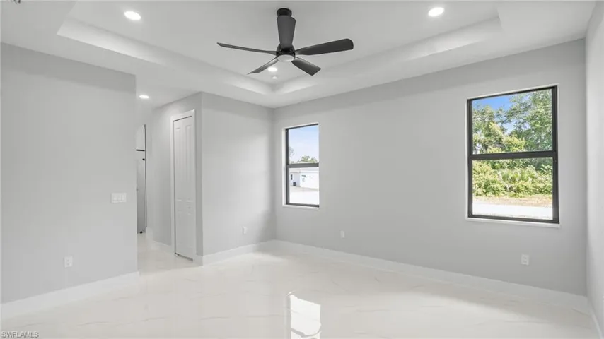 Empty room with recessed lighting, a raised ceiling, healthy amount of natural light, light marble finish flooring, and a ceiling fan