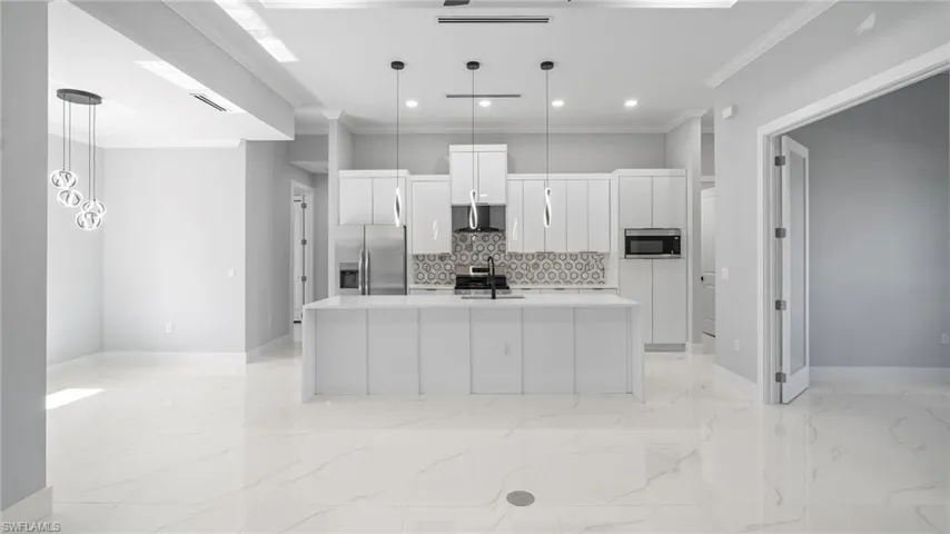 Kitchen featuring appliances with stainless steel finishes, light marble finish flooring, decorative backsplash, white cabinets, and ornamental molding