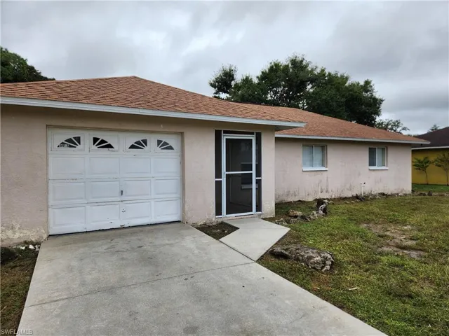 Ranch-style house with stucco siding, a shingled roof, driveway, a garage, and a front yard