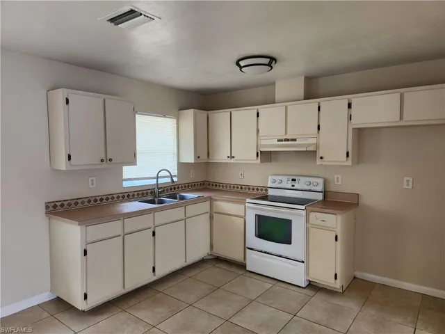 Kitchen with white range with electric cooktop, light tile patterned floors, and under cabinet range hood