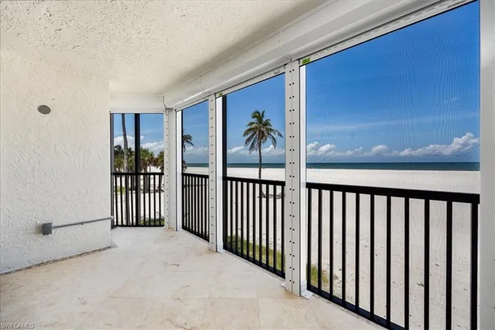 Sunroom featuring view of water and beach, a textured ceiling, and a textured wall