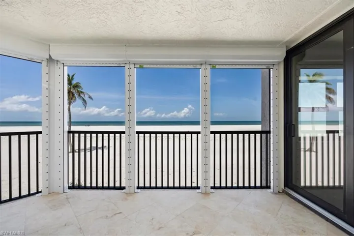 Sunroom with view of water and beach, plenty of natural light, and a textured ceiling