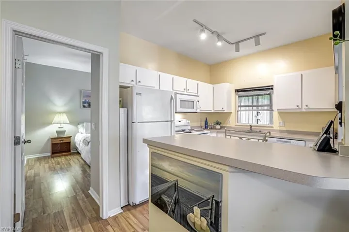 Kitchen featuring white appliances, a peninsula, light wood finished floors, and white cabinets