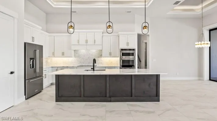 Kitchen with light stone countertops, sink, a stone fireplace, a tray ceiling, and white cabinets