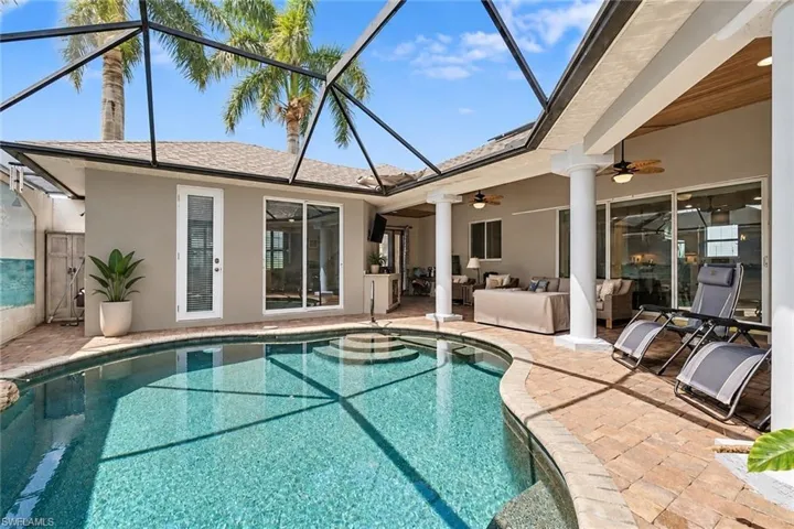 Screened-in pool area featuring a curved swimming pool with integrated steps, a paver deck, and multiple sliding glass doors. Edied with AI