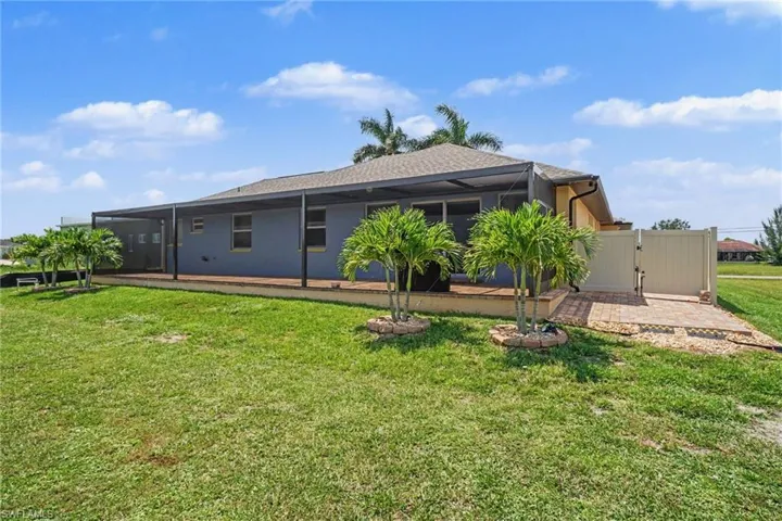Rear exterior featuring a screened lanai with a wood-finish floor, a large grassy area, and mature palm trees